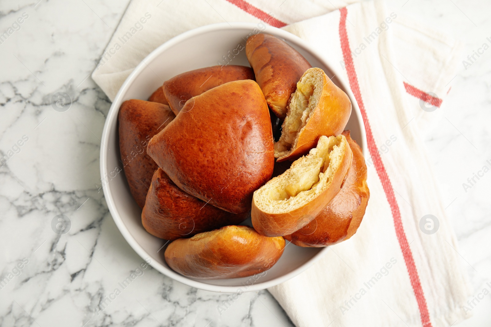 Photo of Delicious baked apple pirozhki in bowl on white marble table, flat lay