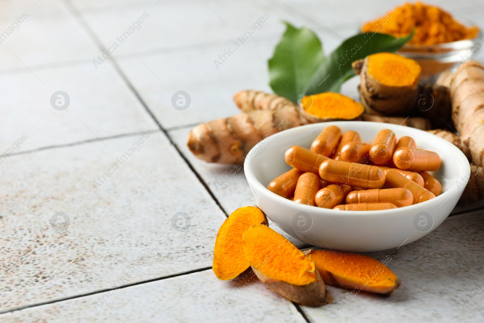 Photo of Turmeric roots and pills on light tiled table. Space for text