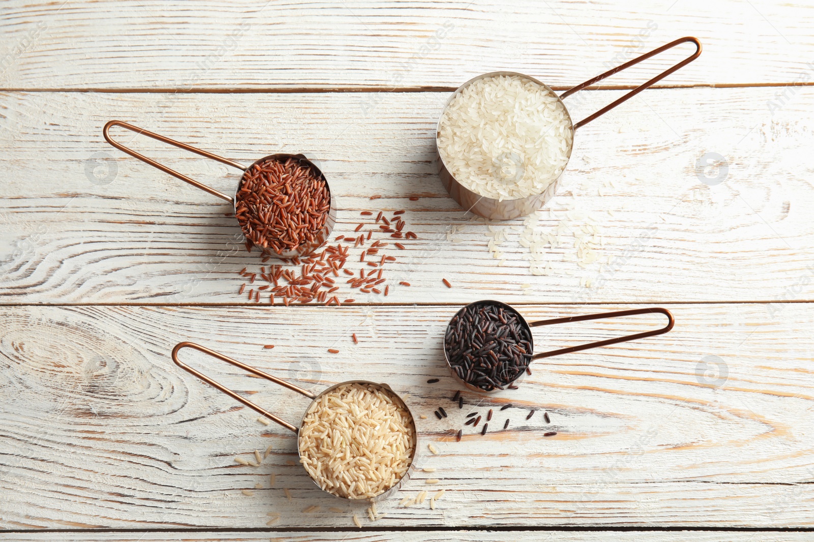 Photo of Measuring cups with different types of rice on white wooden background, top view