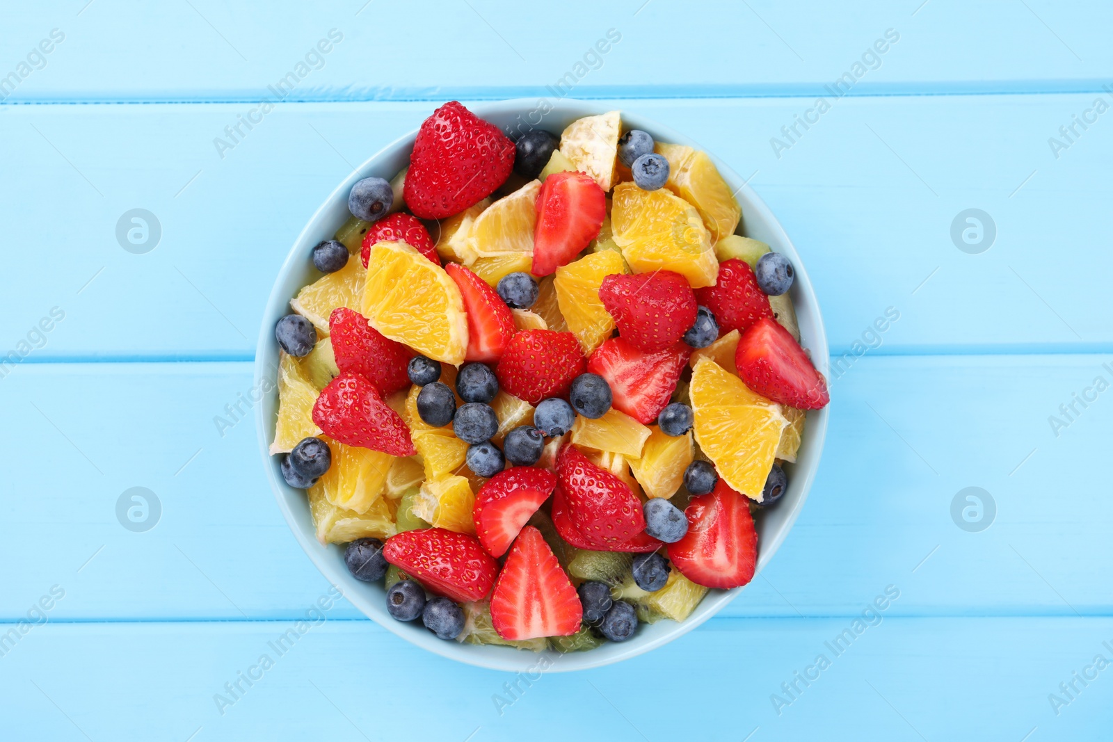 Photo of Delicious fresh fruit salad in bowl on light blue wooden table, top view