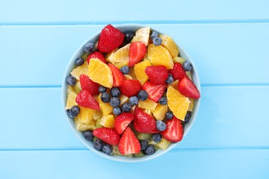 Delicious fresh fruit salad in bowl on light blue wooden table, top view