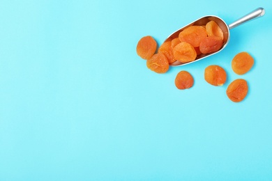 Photo of Scoop of dried apricots on color background, top view with space for text. Healthy fruit