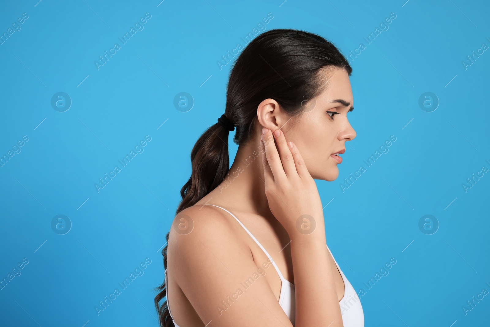 Photo of Young woman suffering from ear pain on light blue background