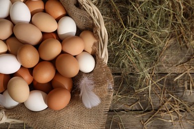 Photo of Fresh chicken eggs in wicker basket and dried hay on wooden table, top view. Space for text