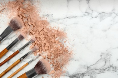 Photo of Makeup brushes and scattered face powder on white marble table, flat lay. Space for text