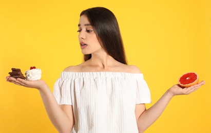 Woman choosing between sweets and grapefruit on yellow background