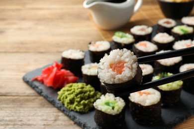 Chopsticks and set of delicious sushi rolls on wooden table, closeup. Space for text