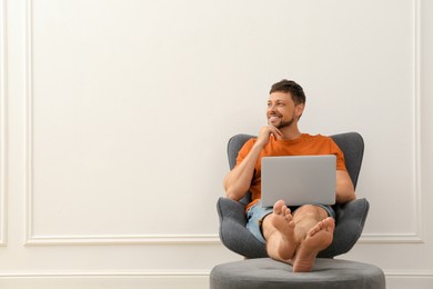 Photo of Happy man using laptop in armchair indoors, space for text. Internet shopping