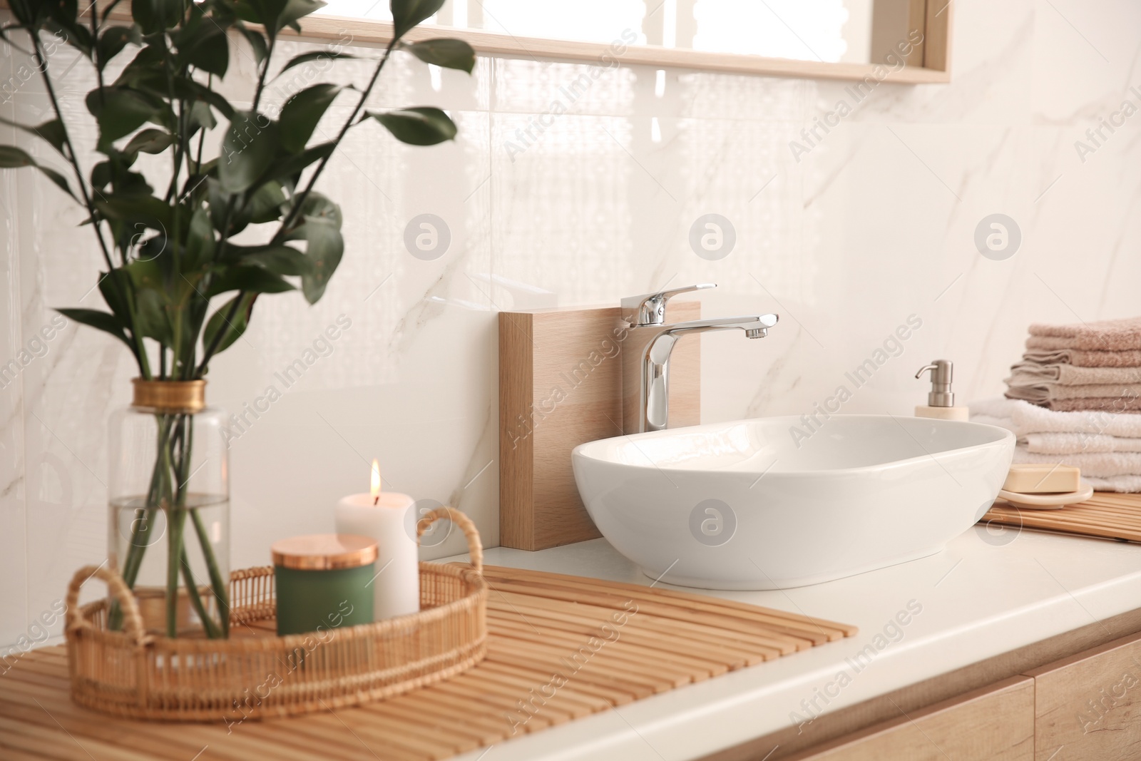 Photo of Vase with beautiful branches, candles and fresh towels near vessel sink in bathroom. Interior design