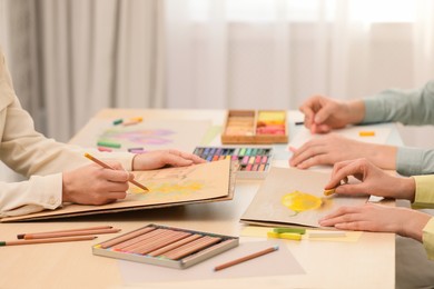 Photo of Artists drawing with soft pastels and pencils at table indoors, closeup