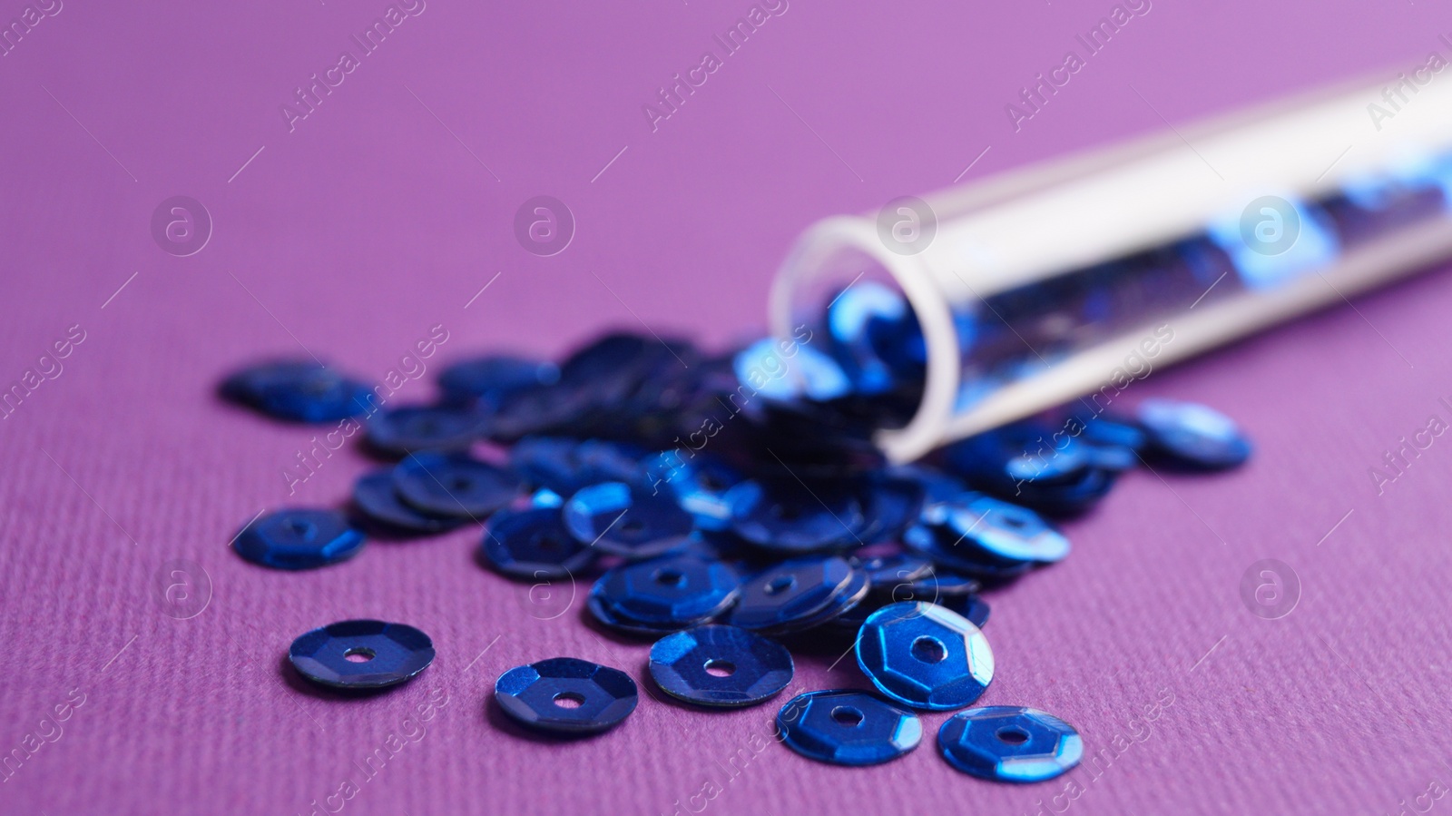 Photo of Tube with many blue sequins on purple background, closeup