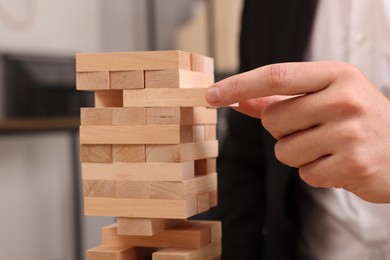 Photo of Playing Jenga. Man removing wooden block from tower indoors, closeup