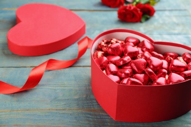 Photo of Heart shaped chocolate candies in gift box and ribbon on blue wooden table, space for text. Valentine's day celebration