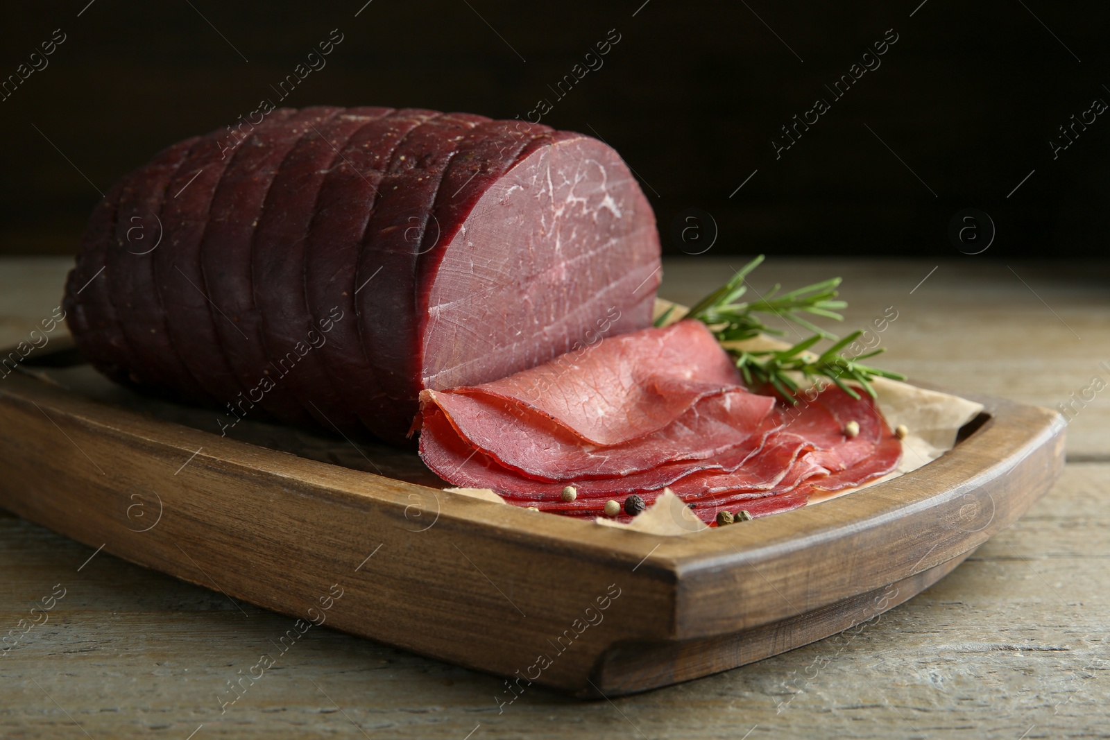 Photo of Tasty bresaola, peppercorns and rosemary on wooden table, closeup