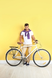 Photo of Handsome young hipster man with bicycle near yellow wall