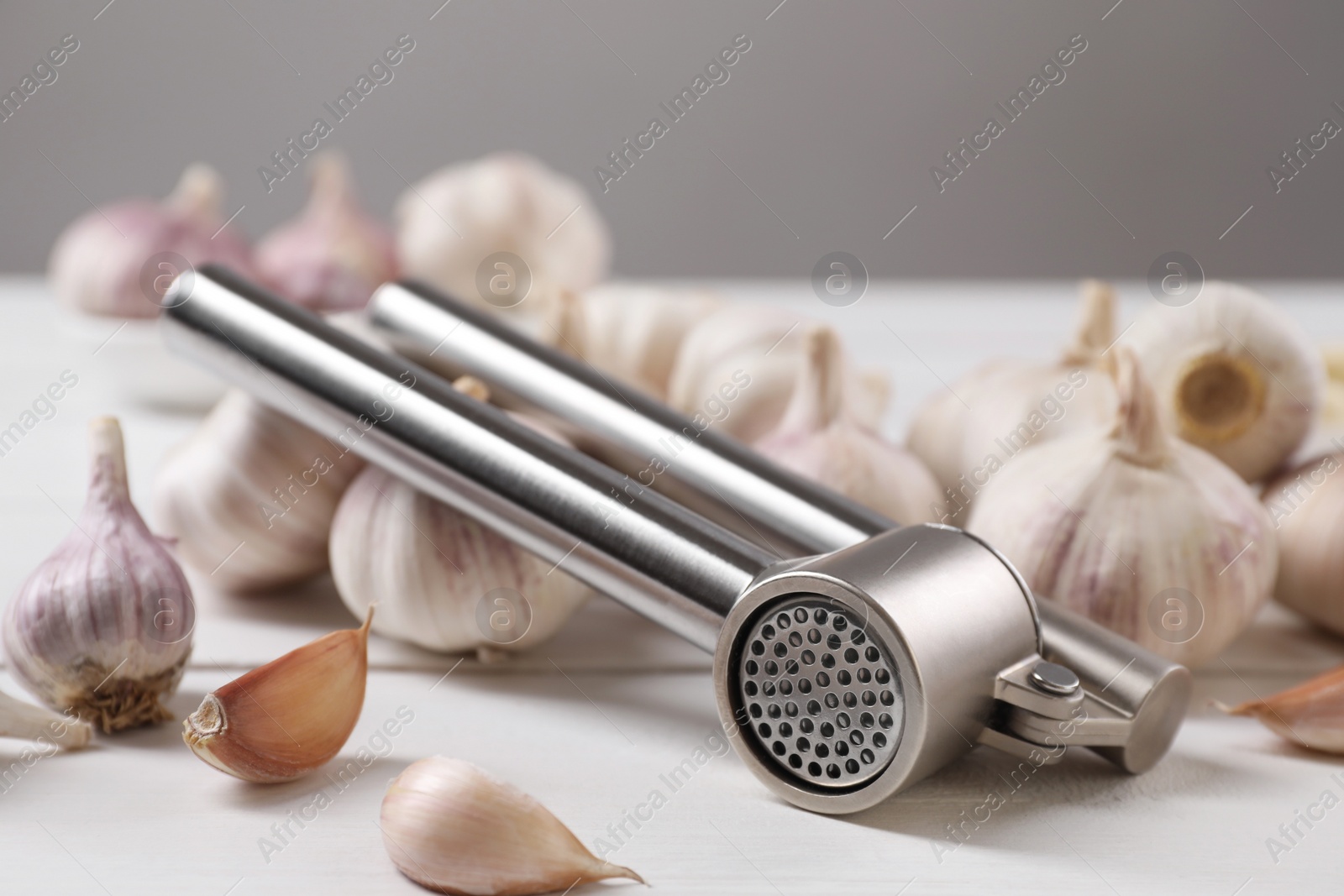 Photo of Metal press and garlic on white table, closeup