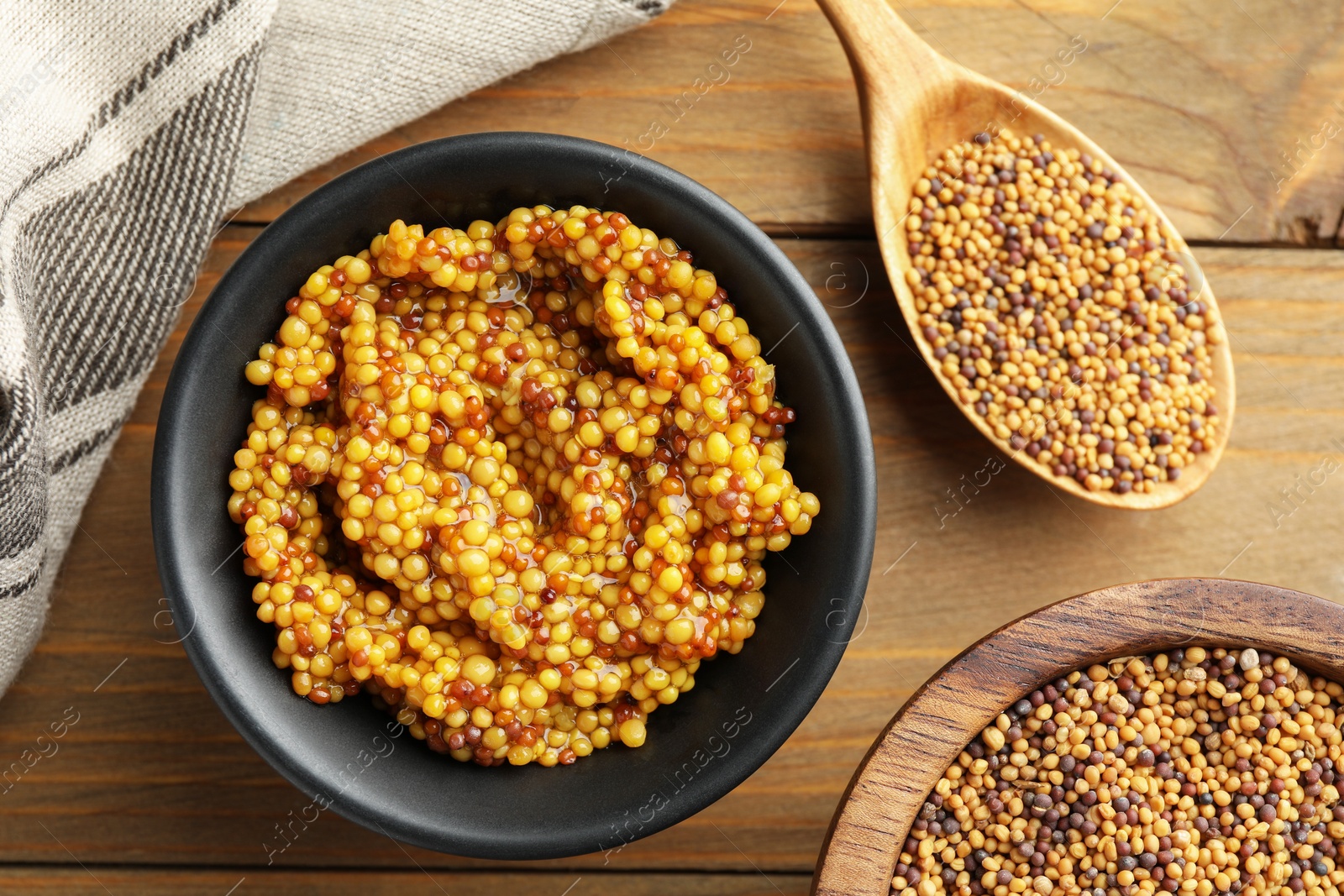 Photo of Whole grain mustard in bowl and dry seeds on wooden table, flat lay