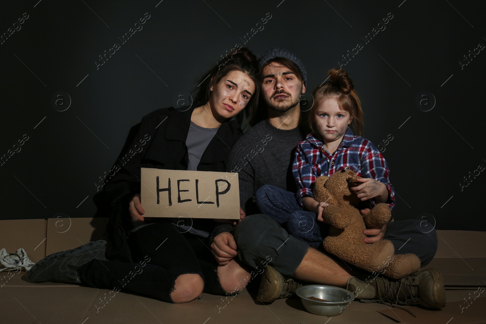 Photo of Poor family with HELP sign on floor near dark wall