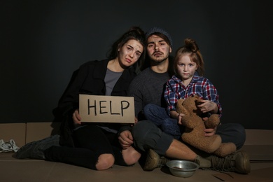 Poor family with HELP sign on floor near dark wall