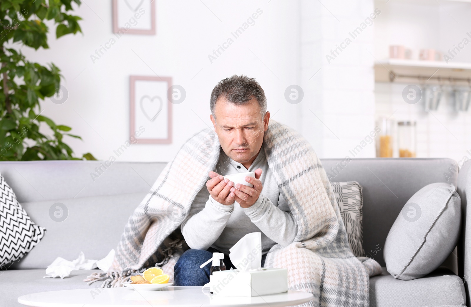 Photo of Man with cup of tea for cough on sofa at home