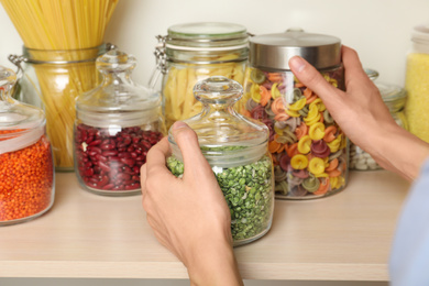 Photo of Woman taking jars of different products from wooden shelf, closeup