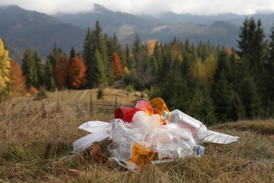 Photo of Pile of plastic garbage on grass against mountain landscape