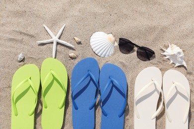 Stylish colorful flip flops, sunglasses, seashells and starfish on sand outdoors, flat lay