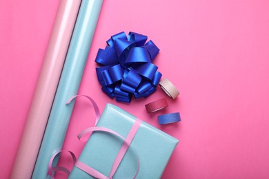 Photo of Rolls of wrapping paper, gift box, bow and ribbons on pink background, flat lay