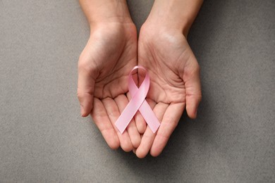 Photo of Woman holding pink ribbon on grey background, top view. Breast cancer awareness concept