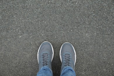 Photo of Man in sneakers standing on asphalt, top view. Space for text