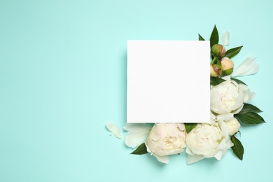 Beautiful white peonies and blank card on turquoise background, flat lay. Space for text