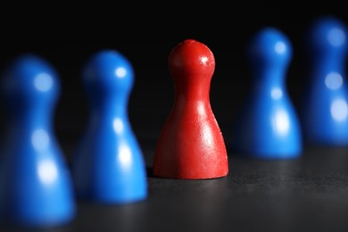 Photo of Choice concept. Red pawn among blue ones on black table, closeup