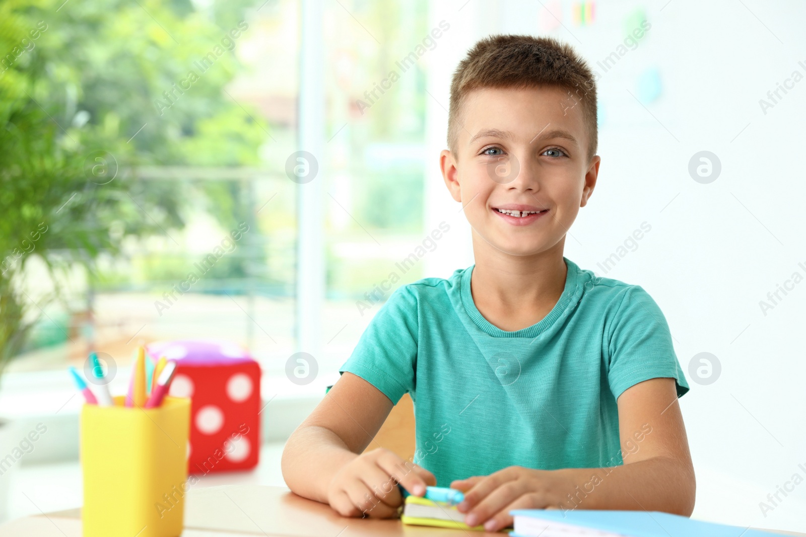 Photo of Little boy with school stationery at desk in classroom