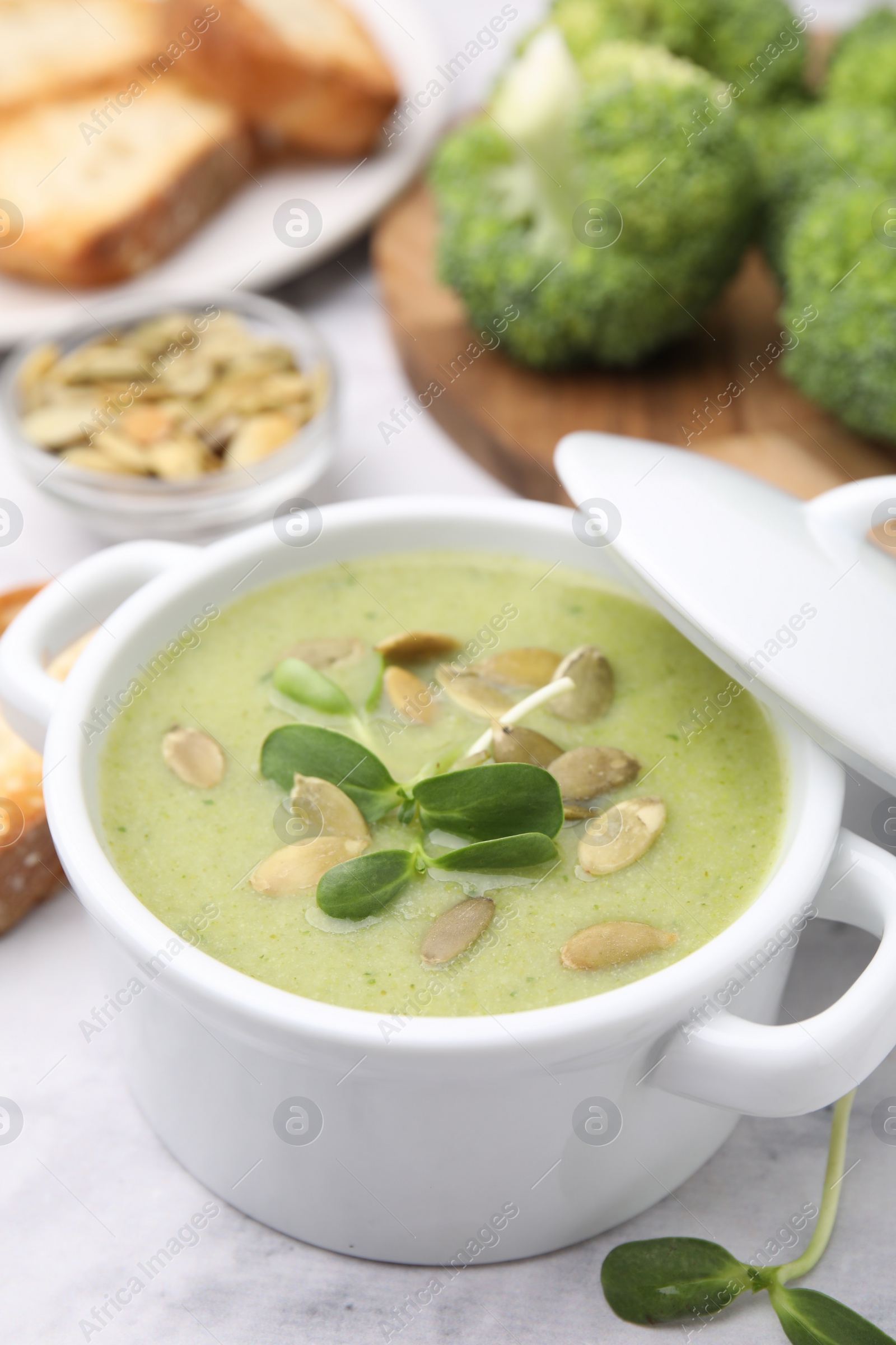 Photo of Delicious broccoli cream soup with pumpkin seeds on white marble table, closeup. Space for text