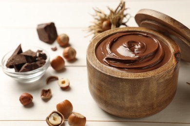 Photo of Bowl of tasty chocolate paste with hazelnuts on white wooden table, space for text