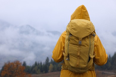 Woman in raincoat with backpack enjoying mountain landscape during rain, back view