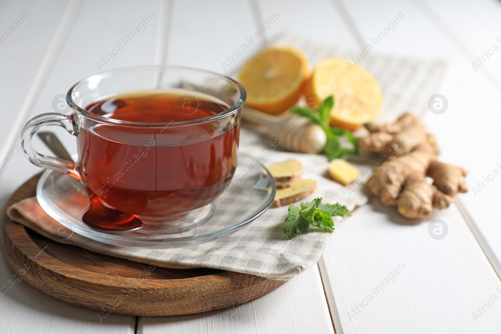 Photo of Cup of delicious ginger tea and ingredients on white wooden table, closeup. Space for text