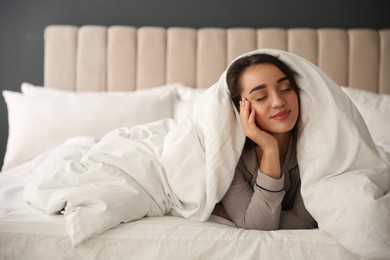 Photo of Beautiful young woman wrapped with soft blanket relaxing in bed at home