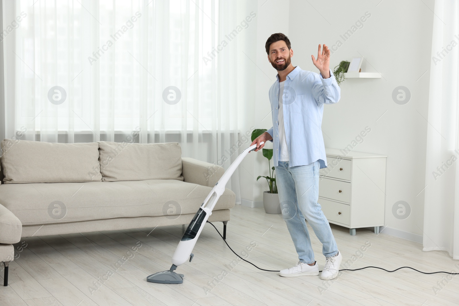 Photo of Happy man cleaning floor with steam mop at home