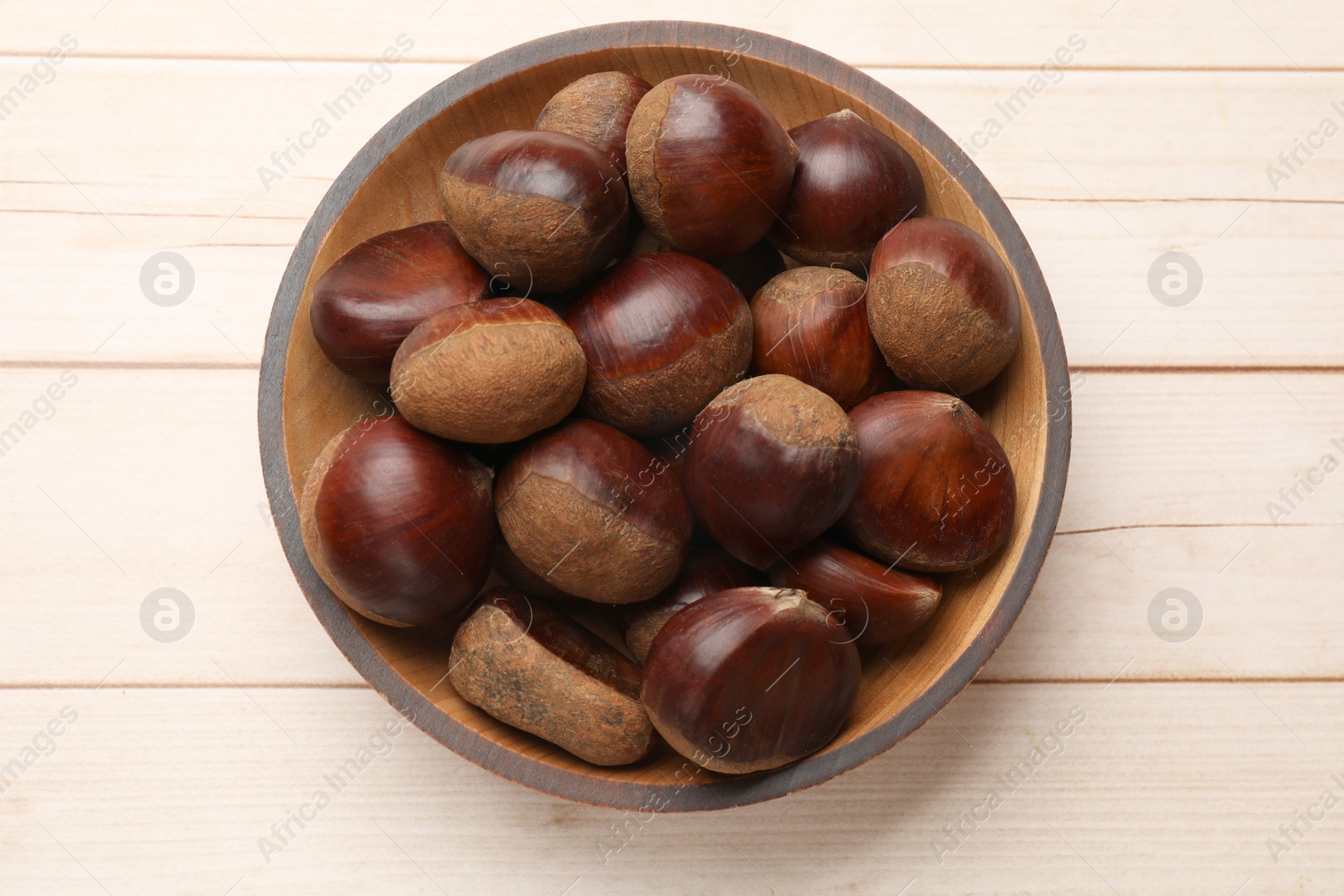 Photo of Sweet fresh edible chestnuts on light wooden table, top view