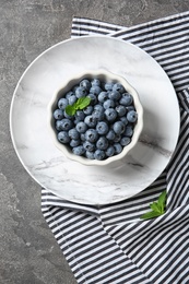 Photo of Dishware with juicy blueberries on color table, top view