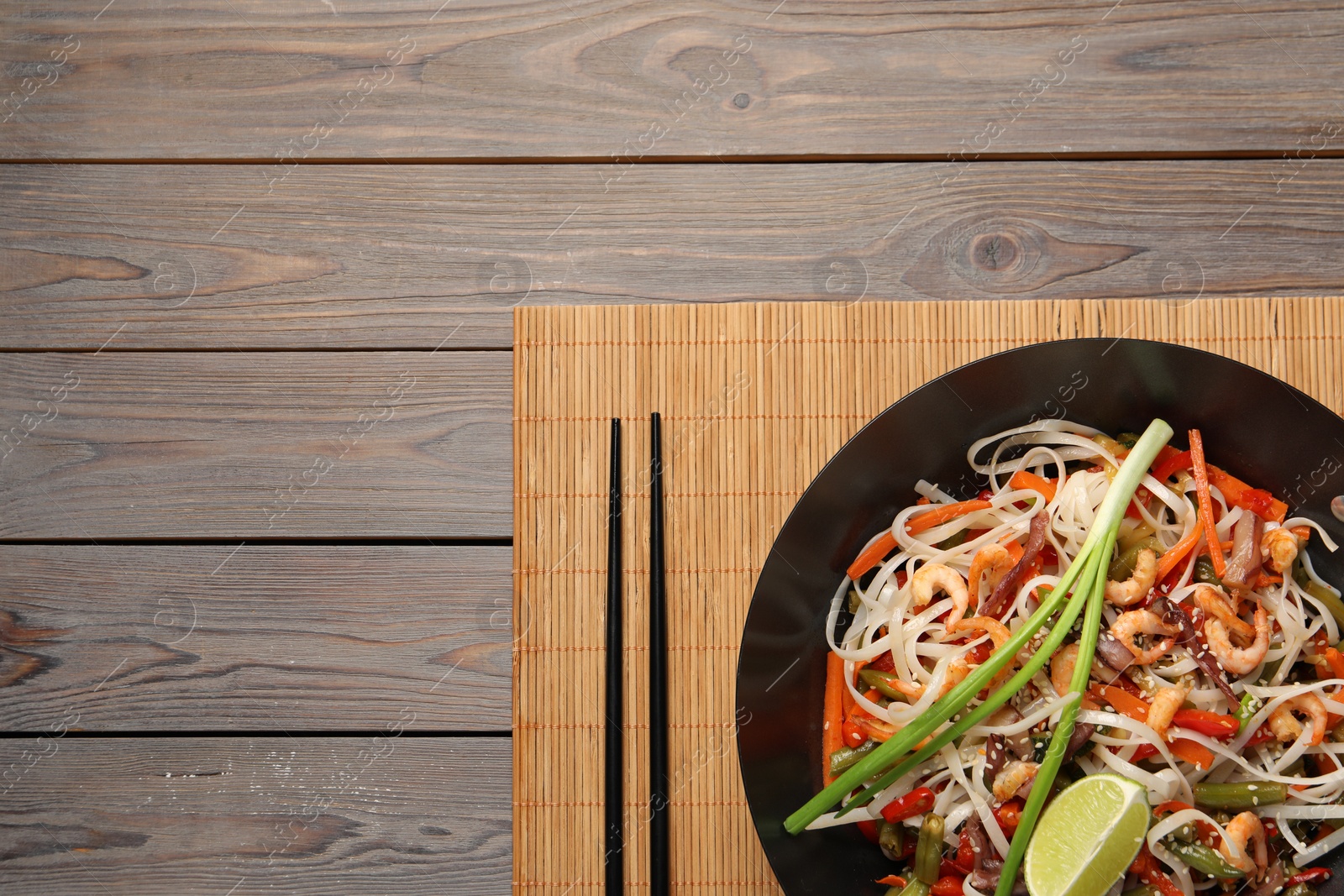 Photo of Shrimp stir fry with noodles and vegetables in wok on wooden table, top view. Space for text