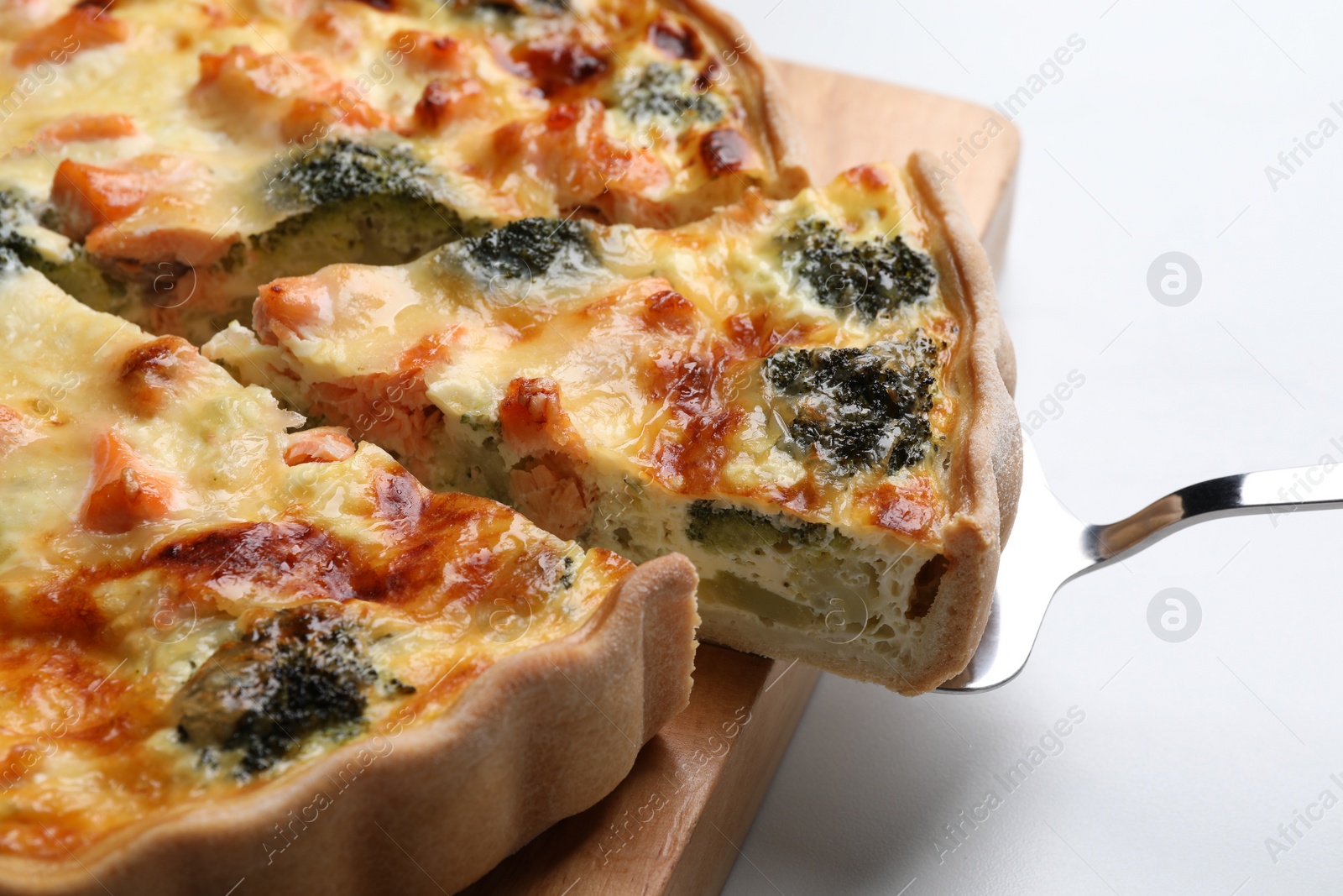 Photo of Taking piece of delicious homemade quiche with salmon and broccoli on white table, closeup