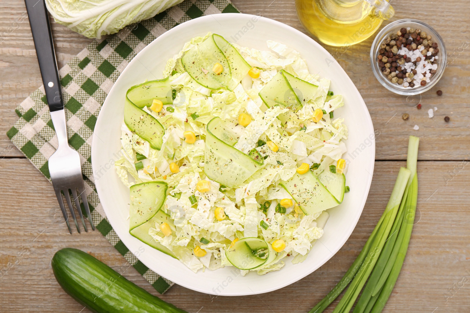 Photo of Tasty salad with Chinese cabbage in bowl and ingredients on wooden table, flat lay