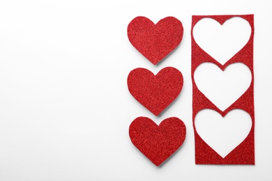 Photo of Red shiny paper hearts and stencil on white background, top view