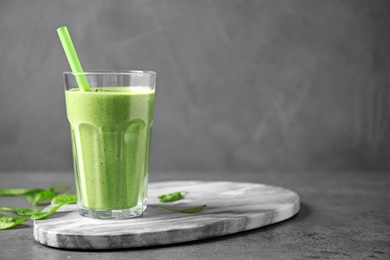 Glass of healthy green smoothie with fresh spinach on grey table, space for text