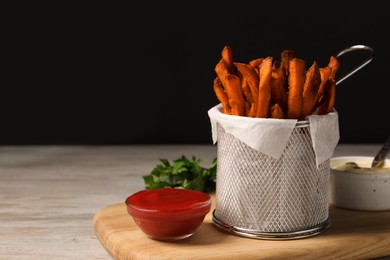 Photo of Frying basket with sweet potato fries, sauces and parsley on table. Space for text