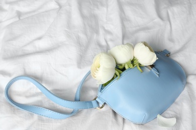 Photo of Stylish bump bag with spring flowers on crumpled white sheet