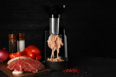 Electric meat grinder with chicken mince and products on black table. Space for text