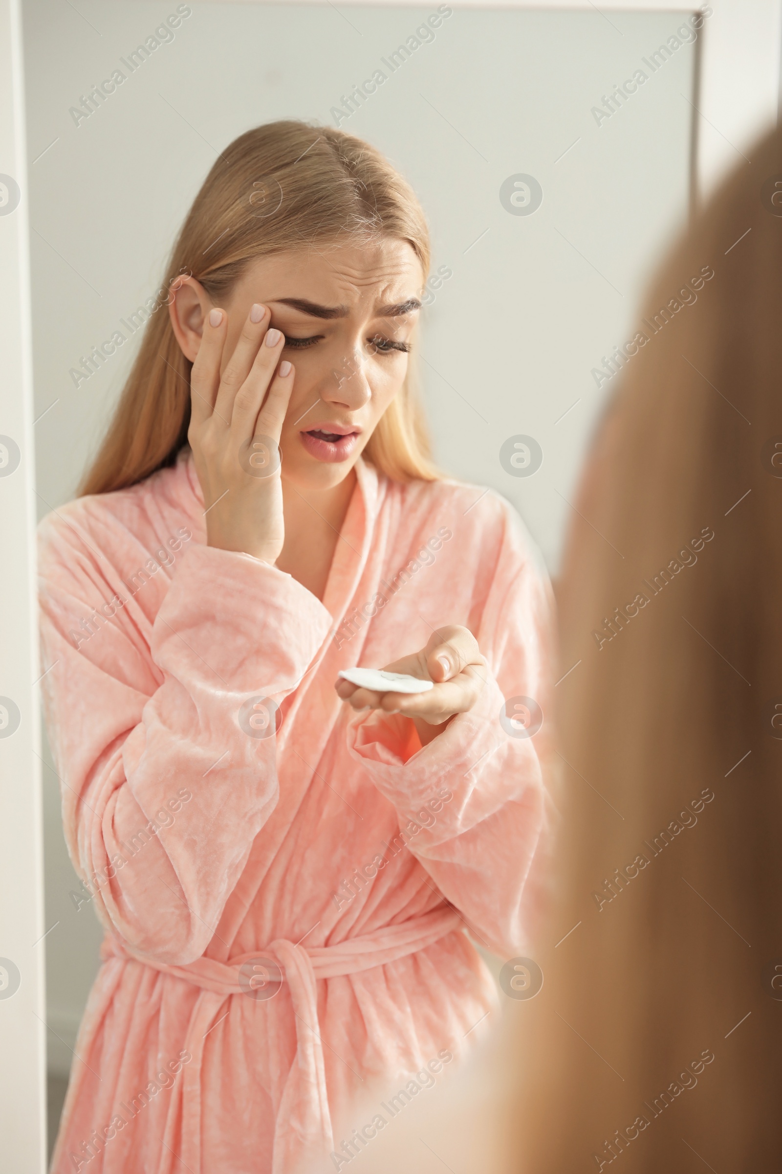 Photo of Young woman with eyelash loss problem near mirror indoors